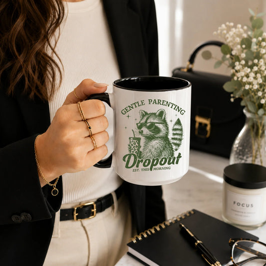 Person holding a white mug with a raccoon graphic and 'Gentle Parenting Dropout' text.