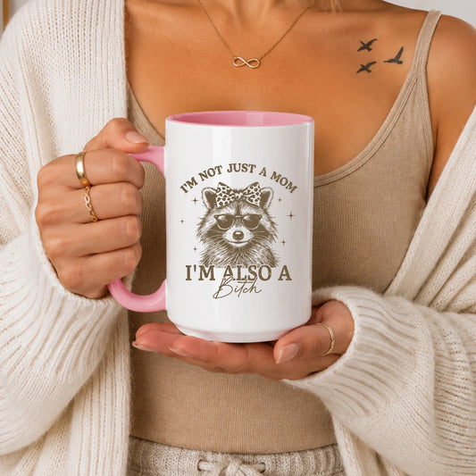 Person holding a white and pink mug featuring a raccoon wearing sunglasses and a bow.